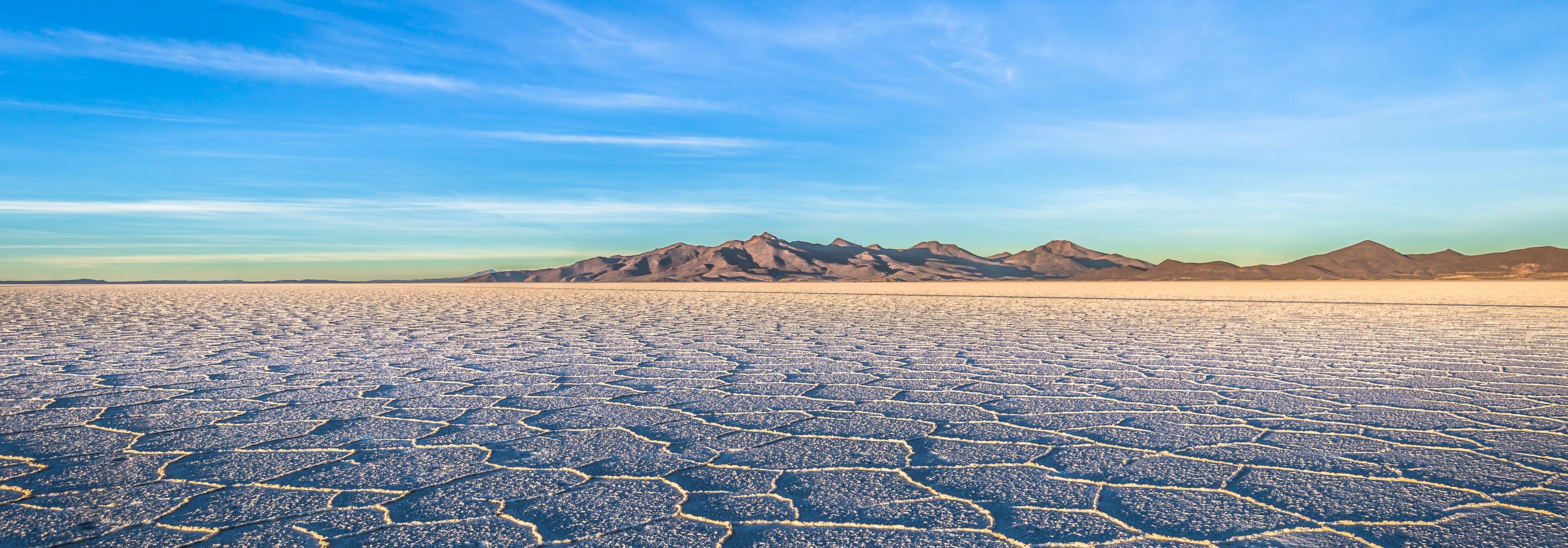 A vast salt flat with hexagonal patterns and distant mountain ranges under a clear sky.