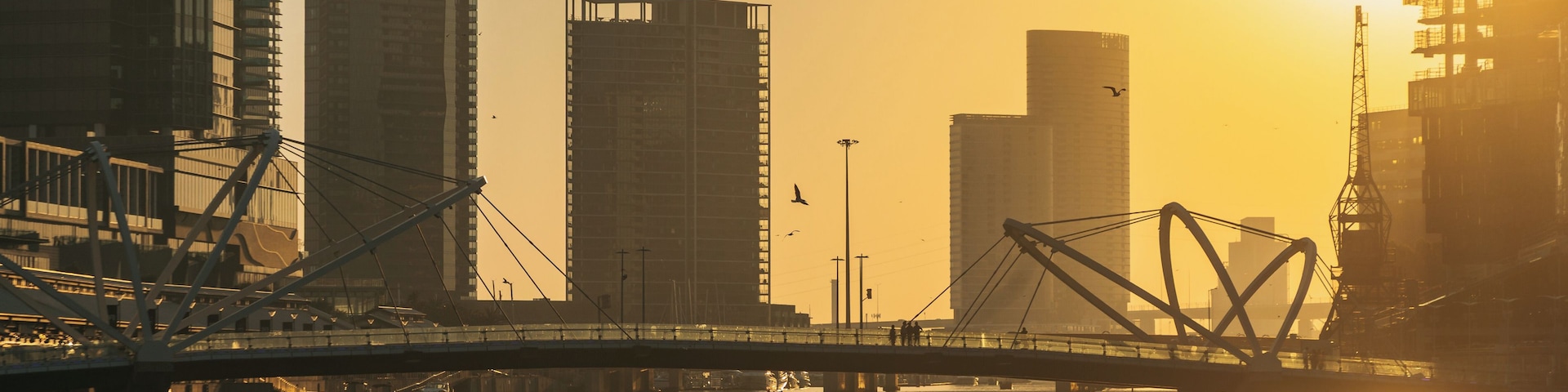 A bridge over a river with tall buildings in the background and the sun setting or rising.