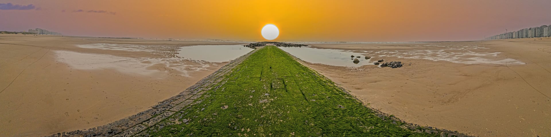Panoramic image along a breakwater on the North Sea beach of the Belgian town Middlekerke with setting sun