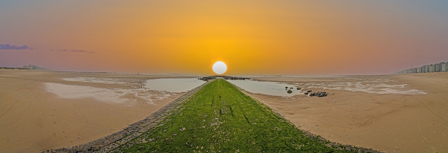 Panoramic image along a breakwater on the North Sea beach of the Belgian town Middlekerke with setting sun