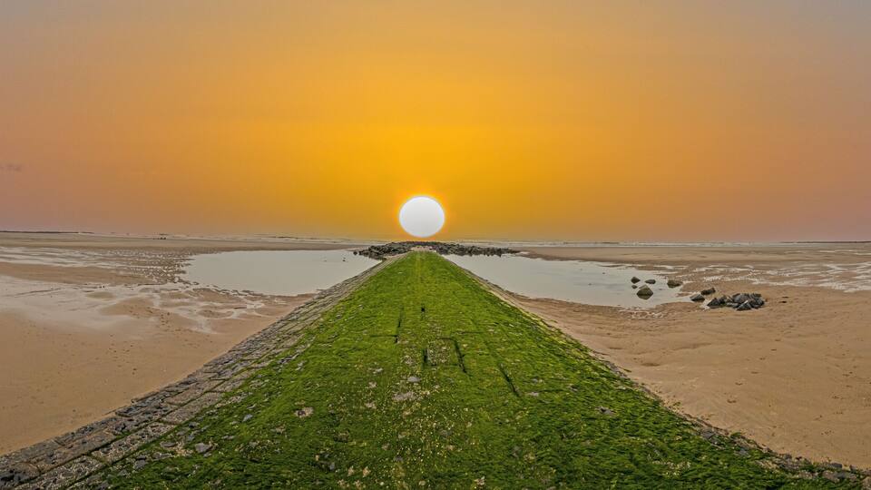 A beach with a long, narrow path leading to a large, round sun.