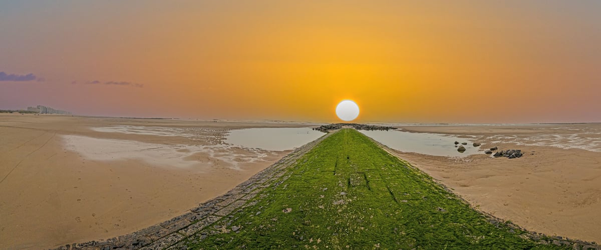 A beach with a long, narrow path leading to a large, round sun.