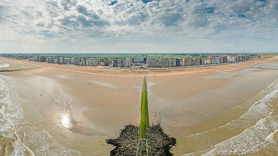 A coastal cityscape with a long pier extending into the sea, surrounded by high-rise buildings and a sandy beach.