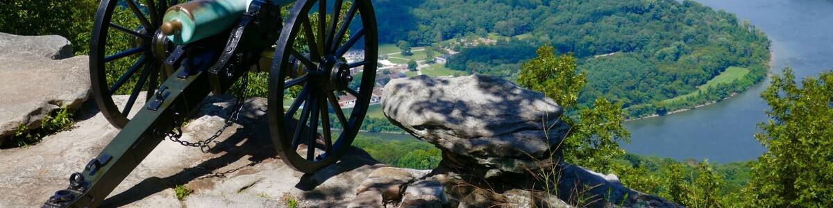 Un canon est installé sur un promontoire rocheux, d’où il domine une rivière et une ville.