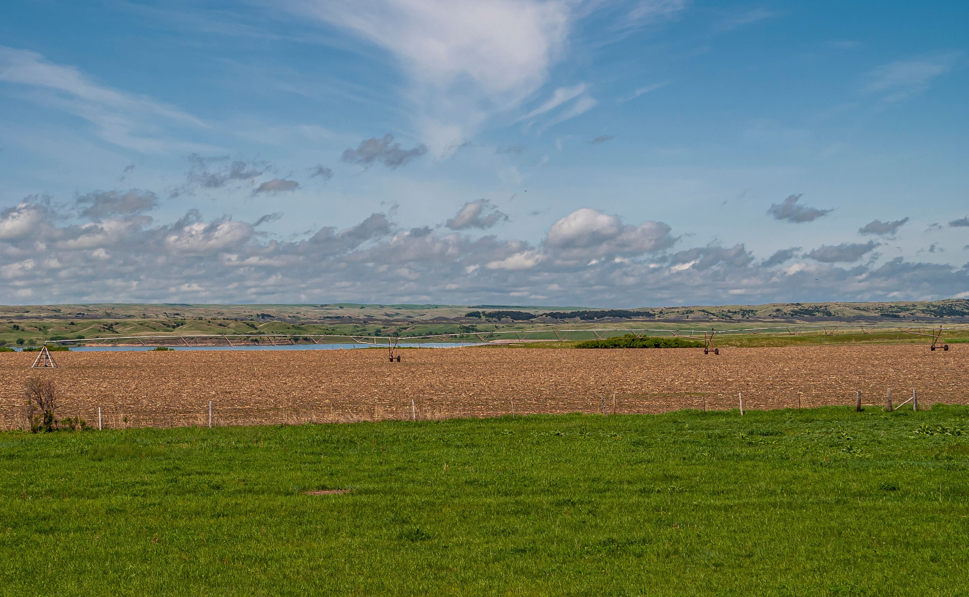 Chamberlain, SD, USA - June 2, 2008: Missouri River North of town. Large irrigation system on wheels stands on brown dirt farmland along shore under blue cloudscape and grass up front.