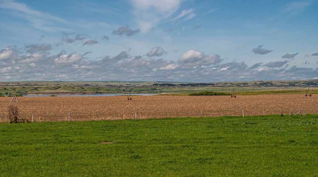 Chamberlain, SD, USA - June 2, 2008: Missouri River North of town. Large irrigation system on wheels stands on brown dirt farmland along shore under blue cloudscape and grass up front.