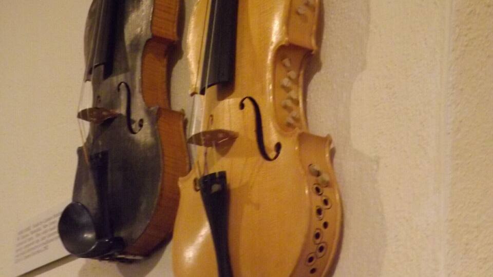 Two violins mounted on a wall with a label below them.