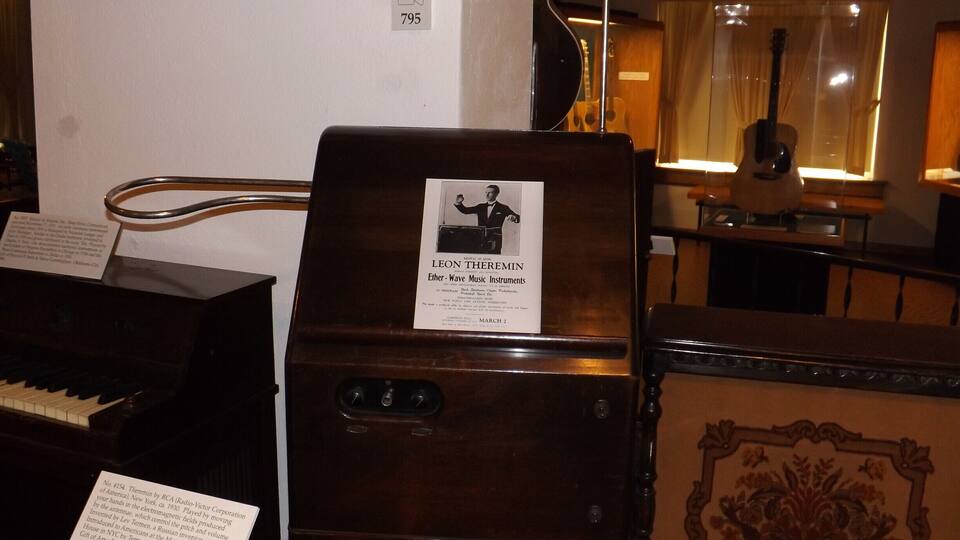 A vintage theremin with a label, a grand piano, and a decorative panel.