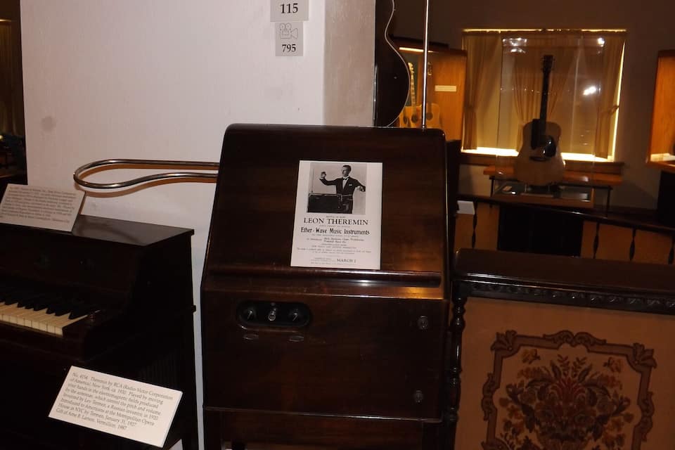 A vintage theremin with a label, a grand piano, and a decorative panel.