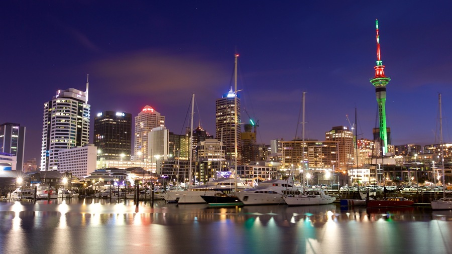 A city skyline at night with illuminated buildings and a prominent tower with red and green lights.