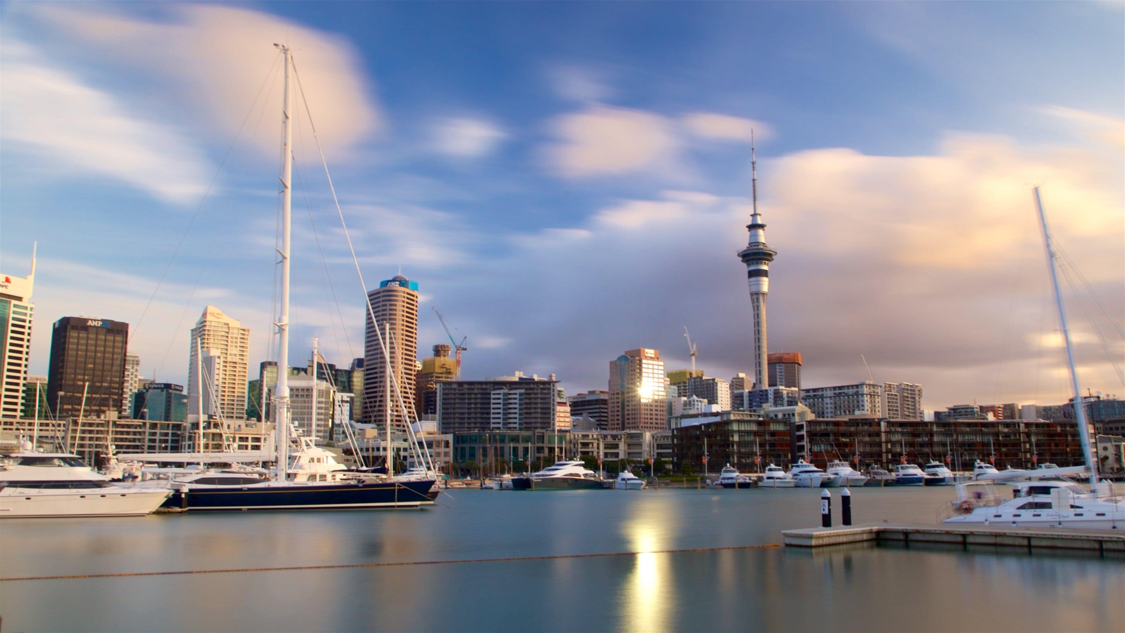 A marina with yachts, a prominent tower, and a city skyline with various buildings.