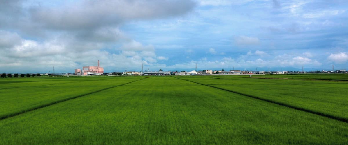 A vast green field with a distant building and a cloudy sky.