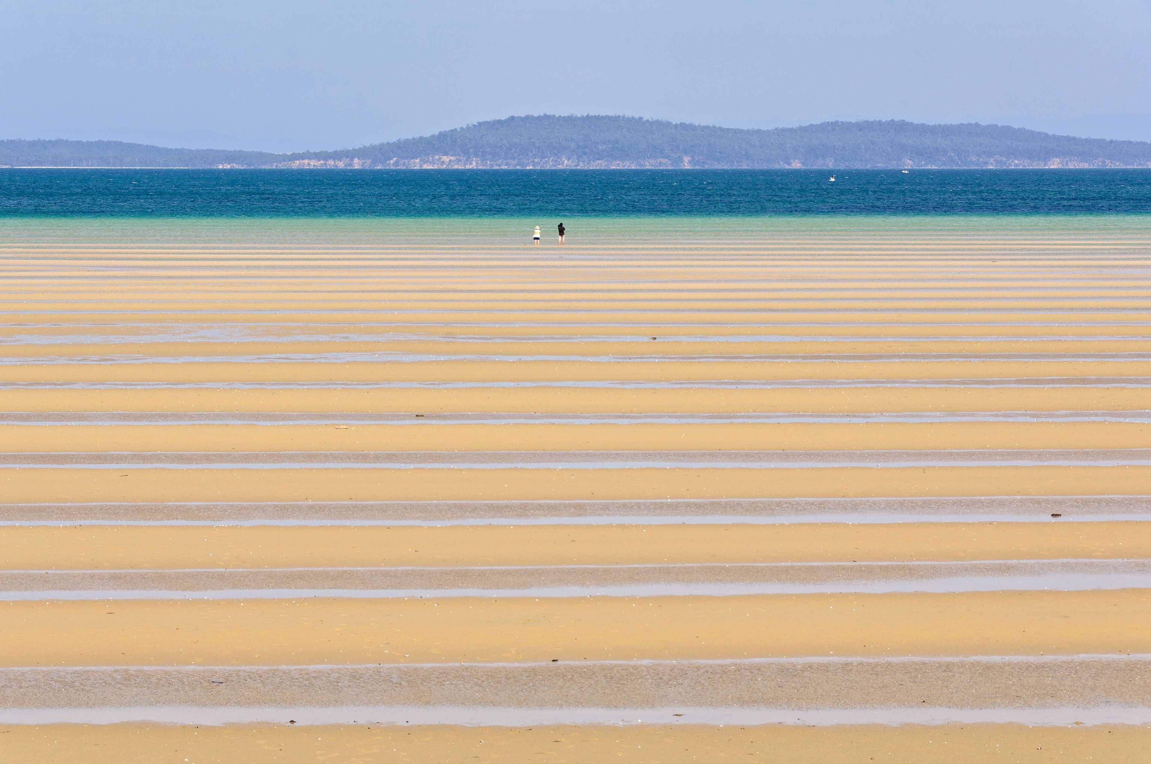 A beach with parallel yellow sand lines and a distant mountain range.