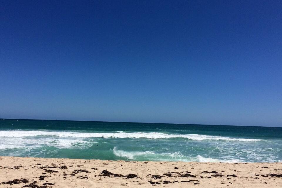 Una platja amb onades que es trenquen a la riba sota un cel blau clar.