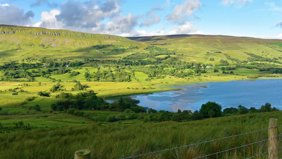 A lush green valley with a river, rolling hills, and scattered houses.