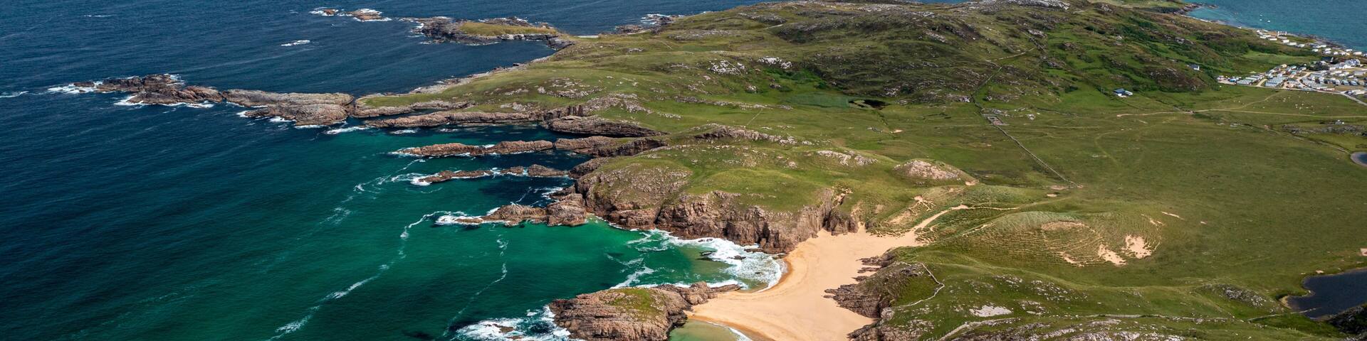 A coastal landscape with a sandy beach, rocky cliffs, and clear blue waters.
