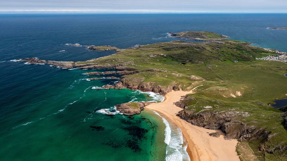 A coastal landscape with a sandy beach, rocky cliffs, and clear blue waters.