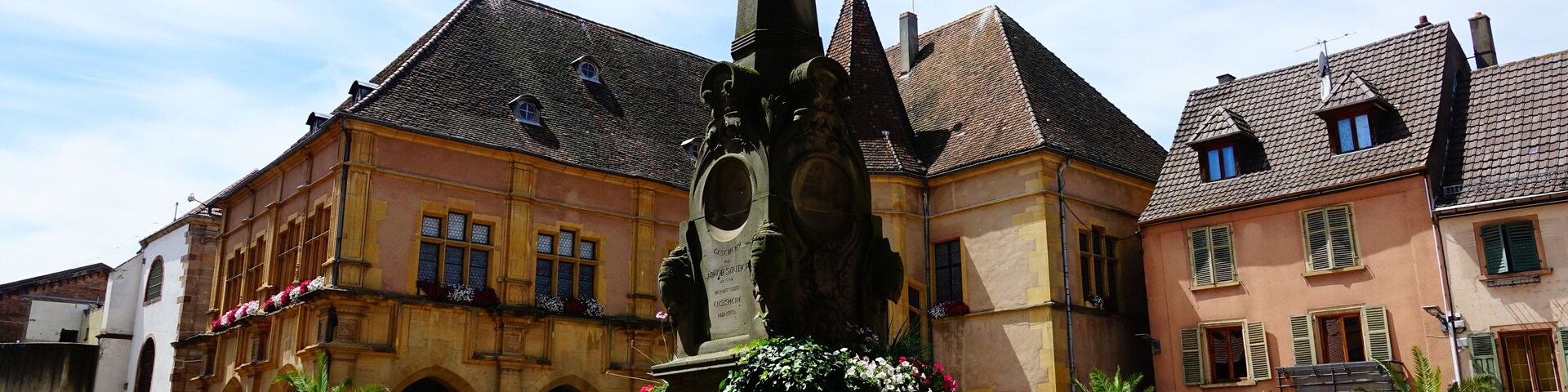 A historic town square with a statue, colorful flowers, and traditional buildings.