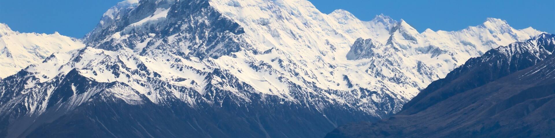 A snow-capped mountain range with a turquoise lake in the foreground.