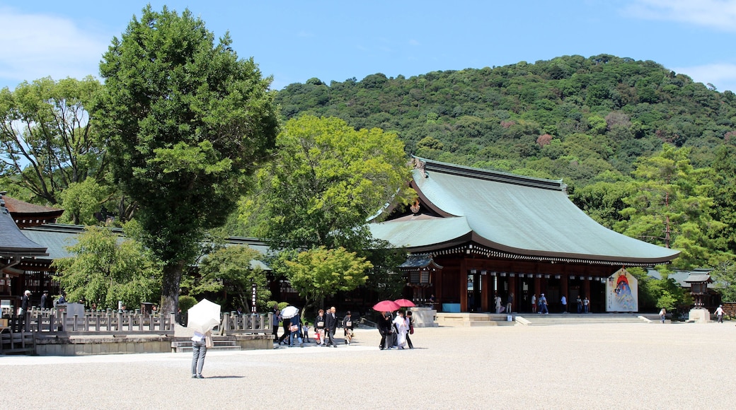 A traditional Japanese temple with a green roof, surrounded by lush greenery and a hilly backdrop.
