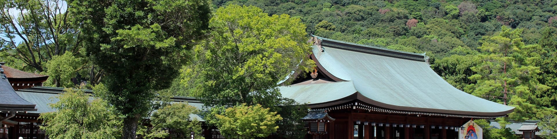 A traditional Japanese temple with a green roof, surrounded by lush greenery and a hilly backdrop.