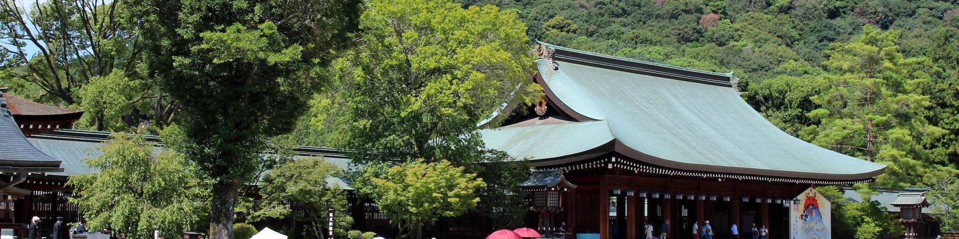 Un templo japonés tradicional con techo verde, rodeado de abundante vegetación y un paisaje montañoso.