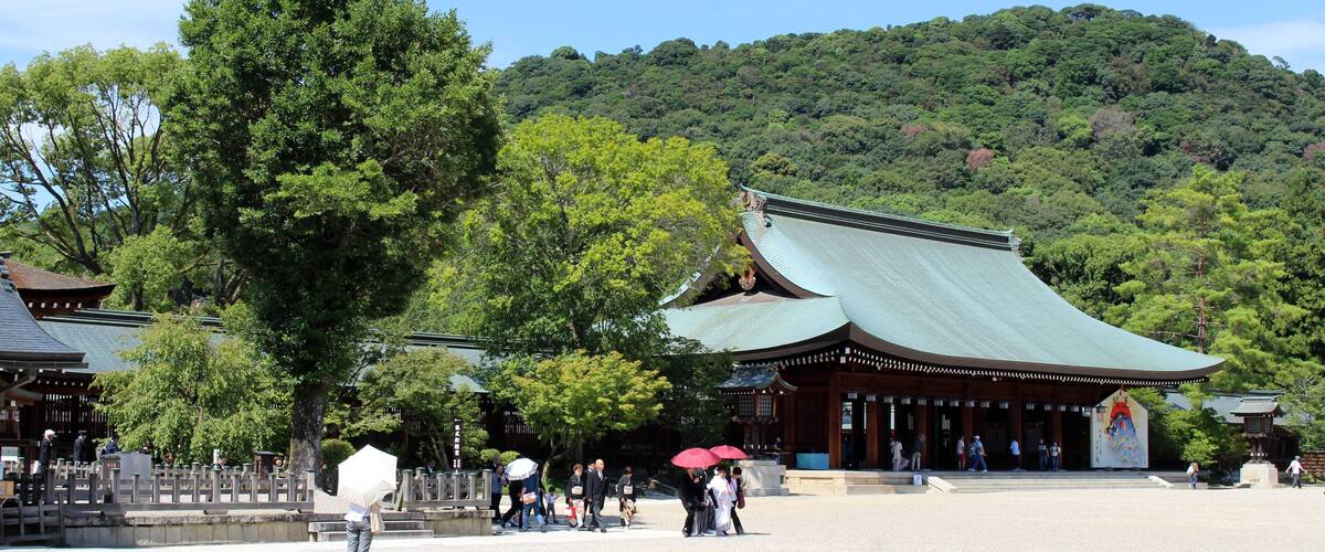 A traditional Japanese temple with a green roof, surrounded by lush greenery and a hilly backdrop.