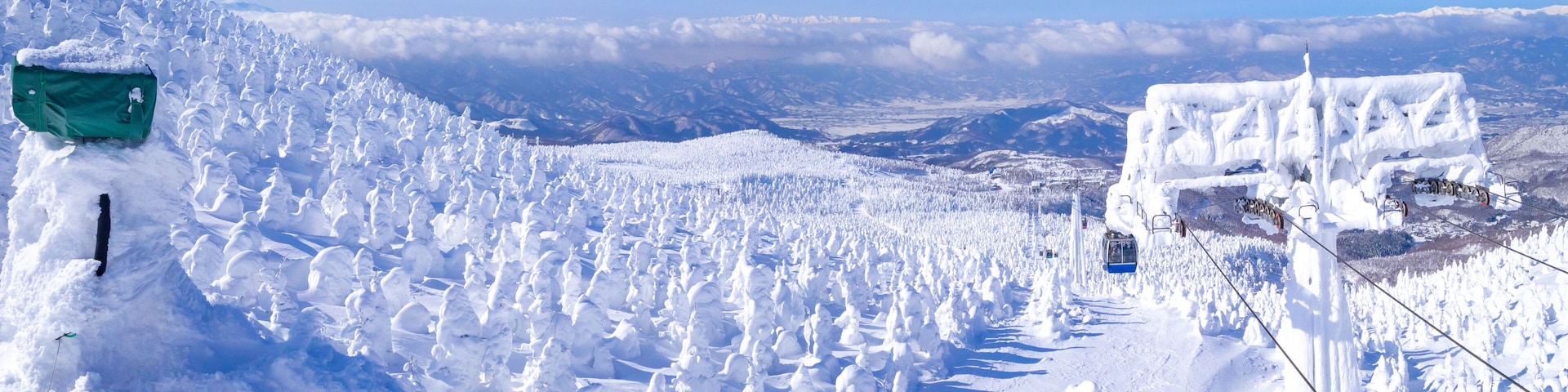 Un paisaje montañoso cubierto de nieve, con un telesilla y un cartel verde.