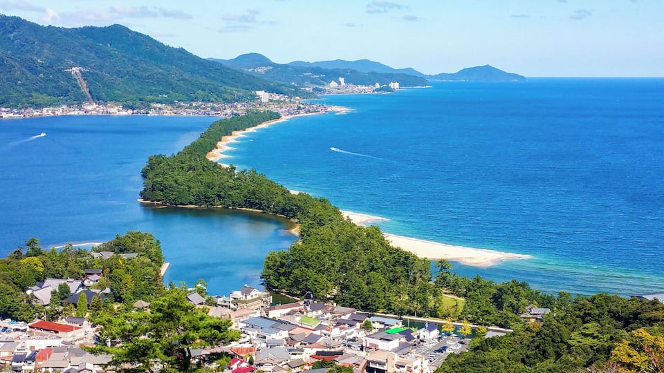 A coastal town with a curving bay, dense forested areas, and a distant mountain range.