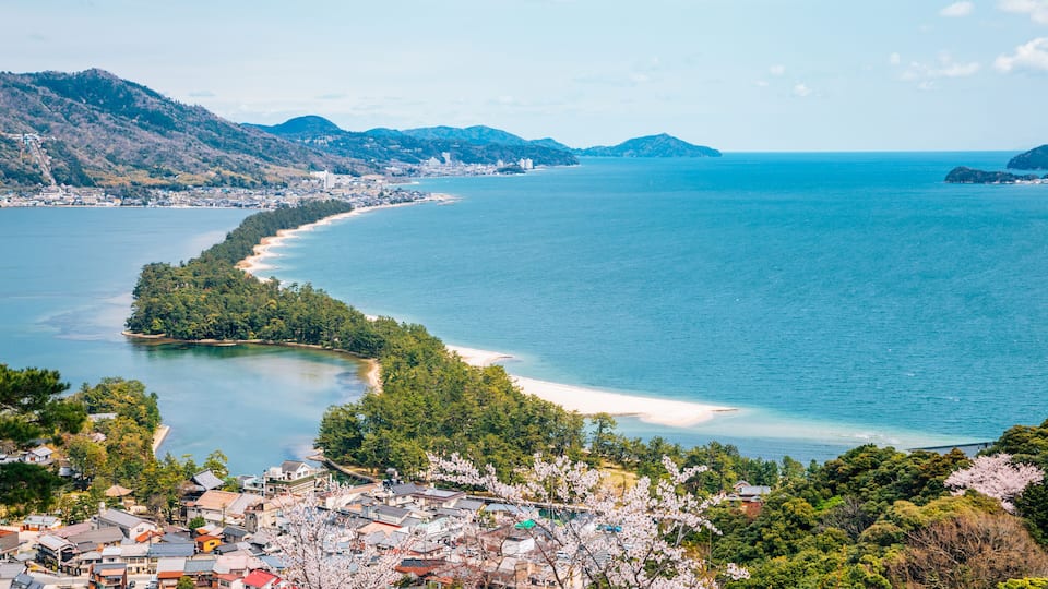 A coastal town with a beach, mountains, and cherry blossoms.