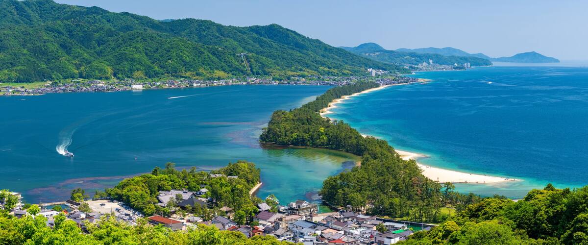 A coastal town with a beach, clear blue waters, and lush green hills.