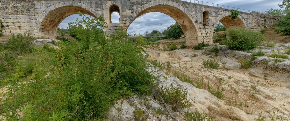 An ancient stone bridge with three arches, surrounded by rocky terrain and sparse vegetation.