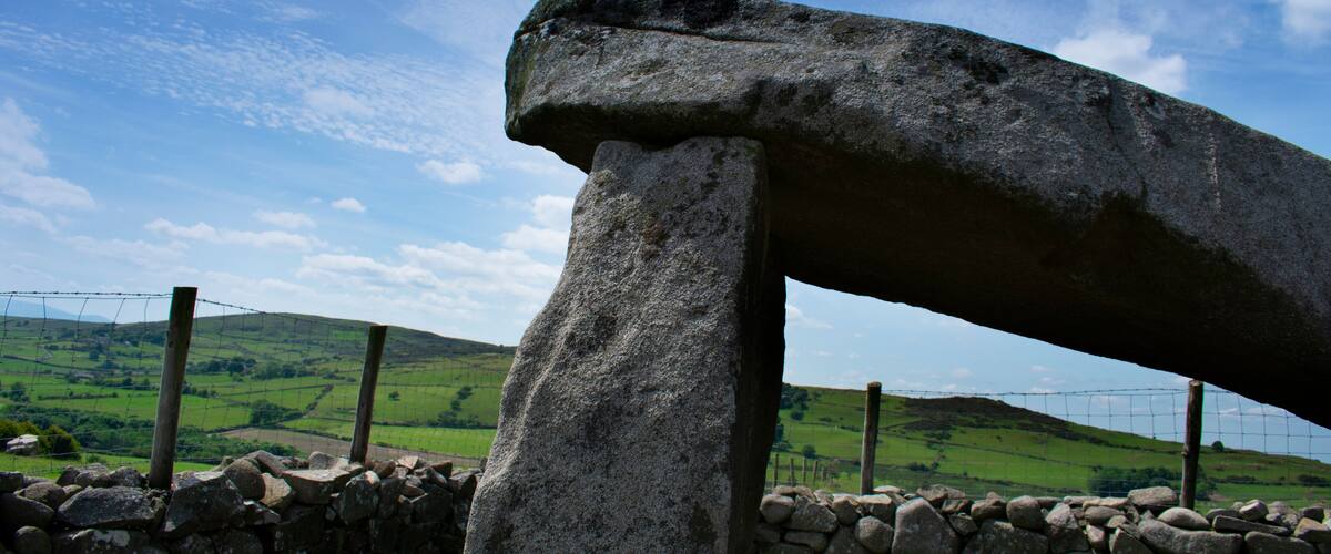 A large stone structure in a rural landscape with a stone wall and a fence.