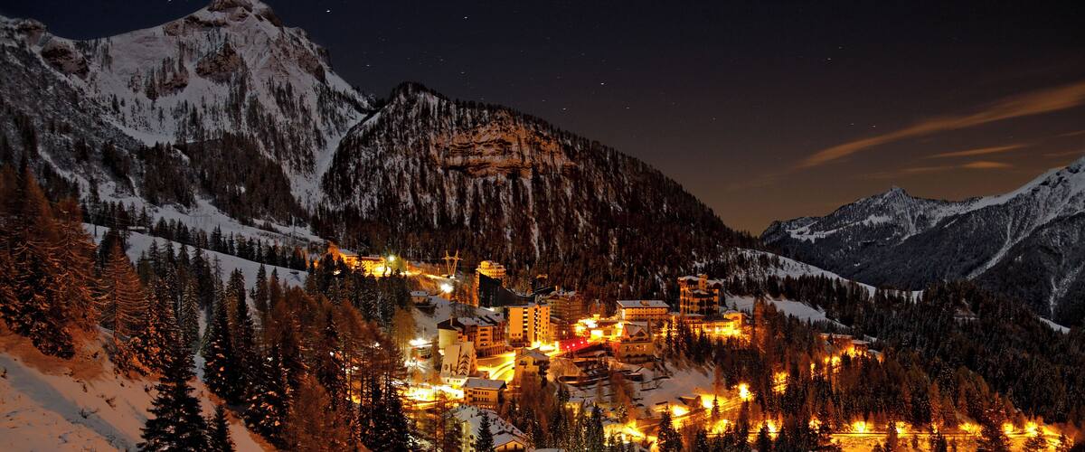 A snow-covered mountain town at night with illuminated buildings and a starry sky.