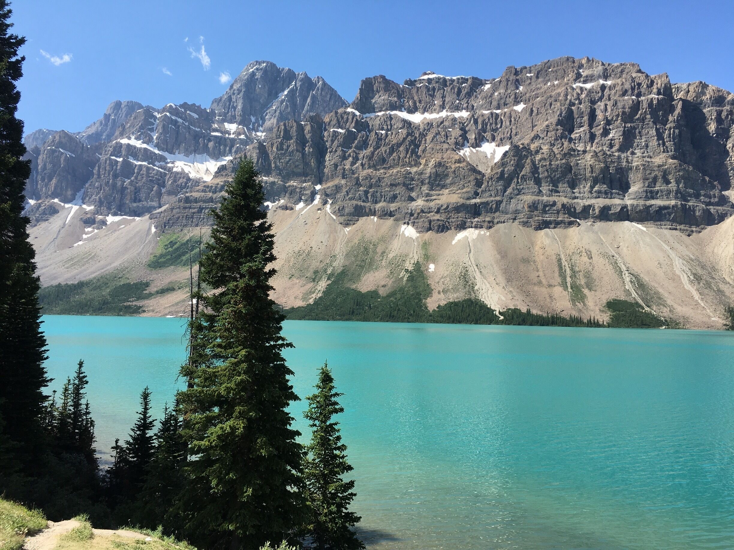 A mountain range with a turquoise lake in the foreground and snow-capped peaks in the background.