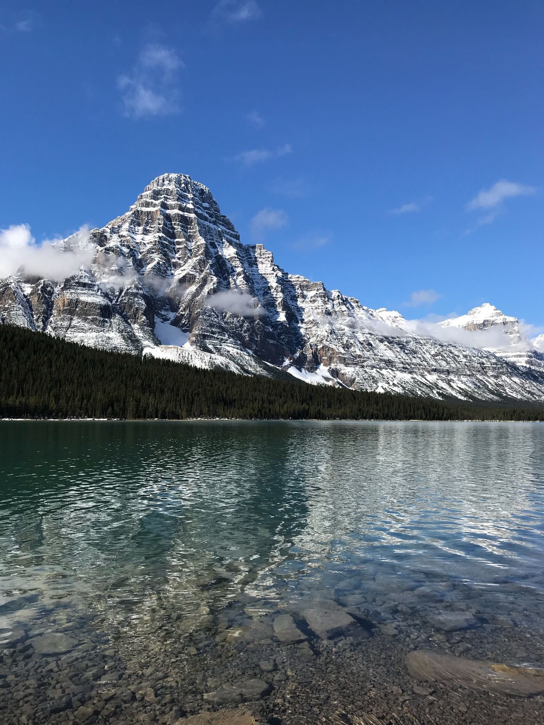 A mountain range with snow-capped peaks, a clear lake, and a forested area.
