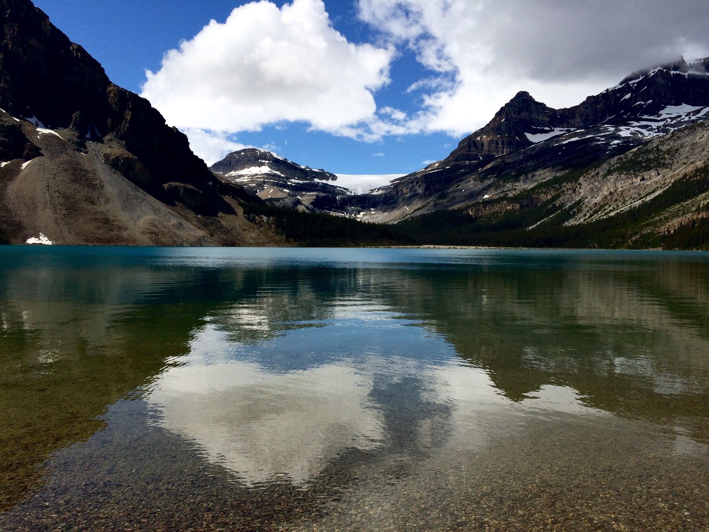 A mountain lake with clear reflections of the surrounding peaks and a partly cloudy sky.