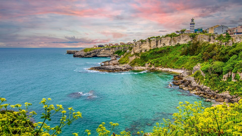 A coastal landscape with a lighthouse, rocky cliffs, and clear turquoise waters.