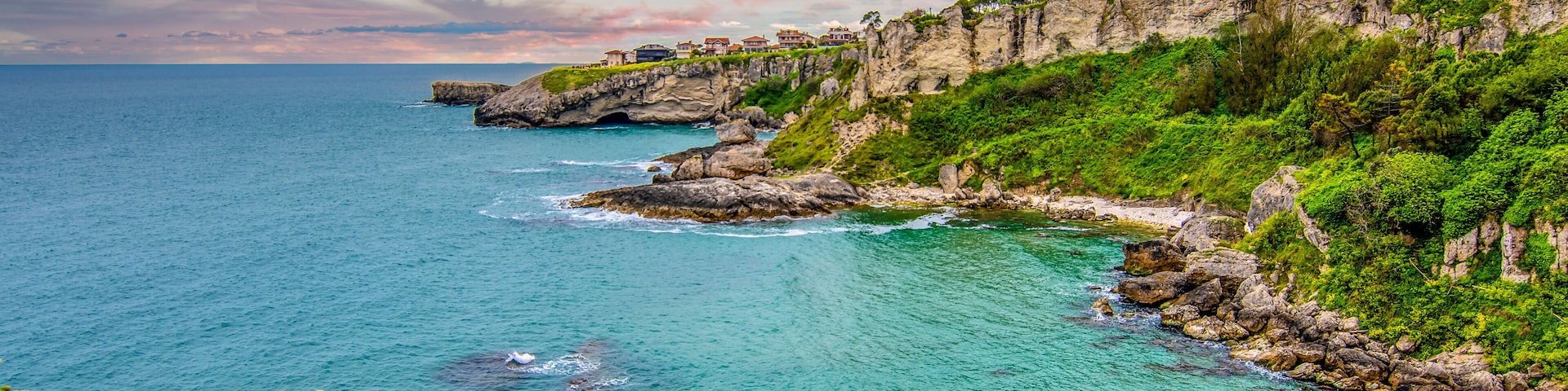 Paisagem costeira com um farol, falésias rochosas e águas turquesa cristalinas.