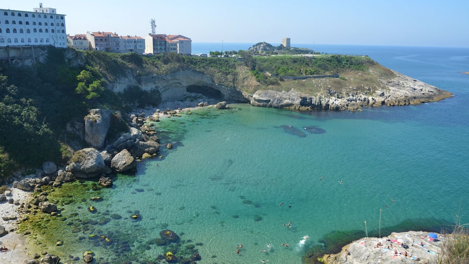 A coastal town with clear waters, rocky shores, and historic buildings.