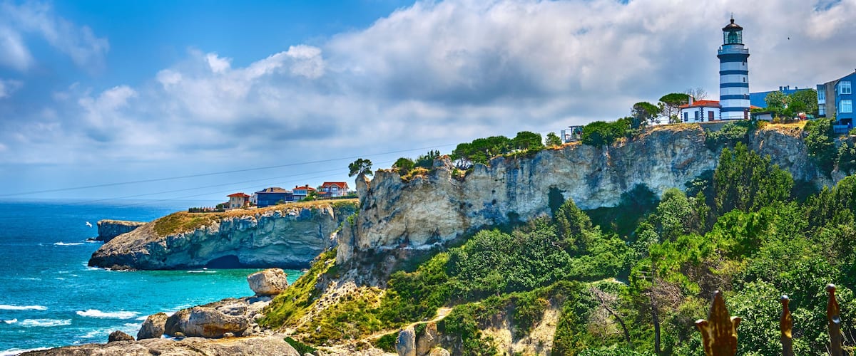 A coastal landscape with a lighthouse, rocky cliffs, and a clear blue sky.