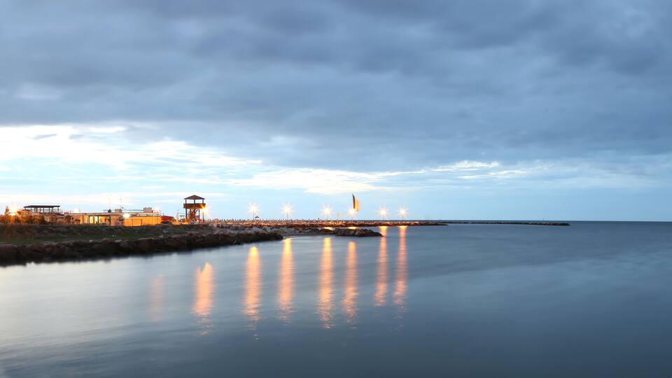 A calm waterfront with a pier, buildings, and a fishing rod.