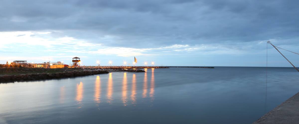 A calm waterfront with a pier, buildings, and a fishing rod.