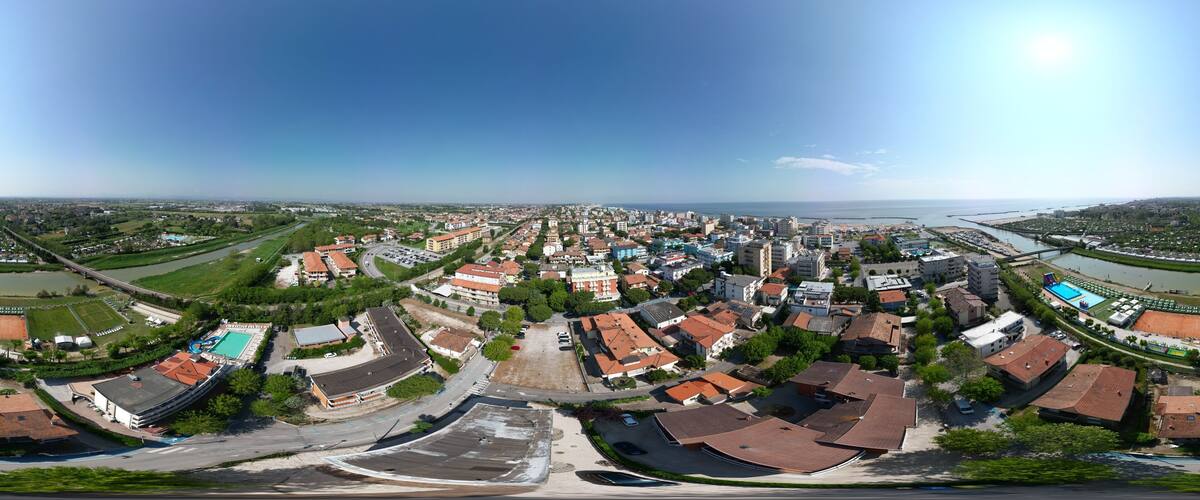 An aerial view of a coastal town with a mix of residential and commercial buildings, a large swimming pool, and a bridge connecting to the mainland.