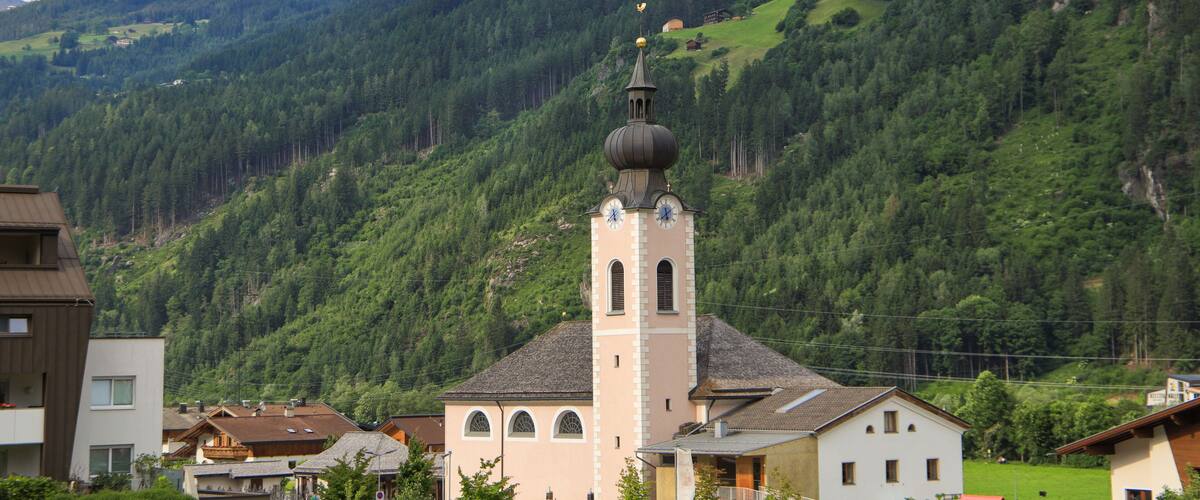 A church with a bell tower, surrounded by lush green hills and a clear sky.
