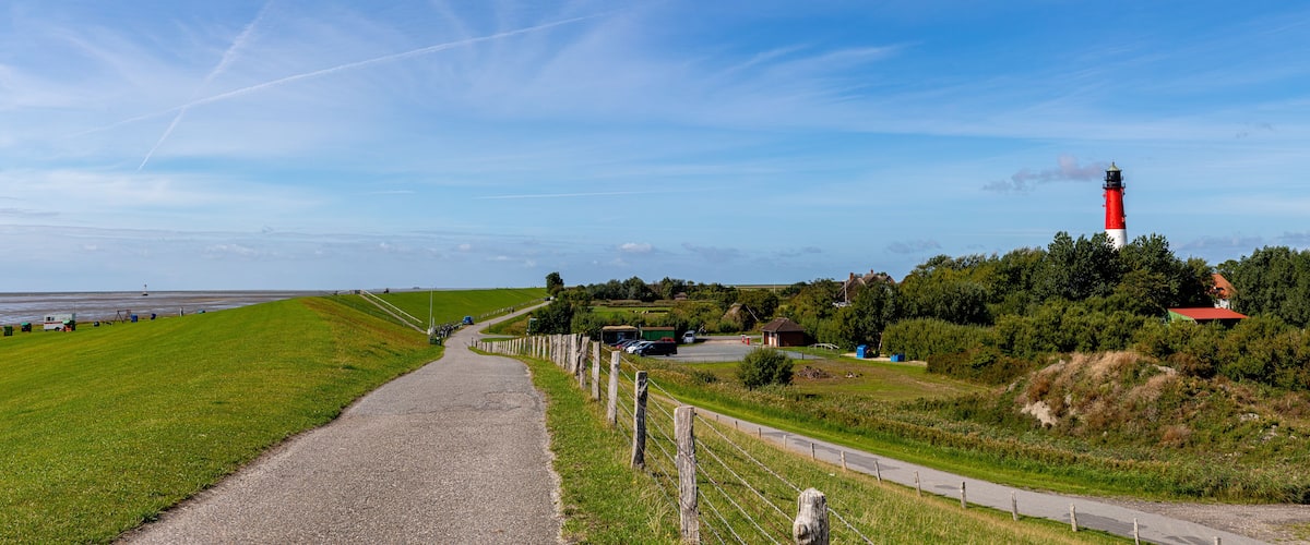 A coastal road with a lighthouse, green fields, and a clear sky.