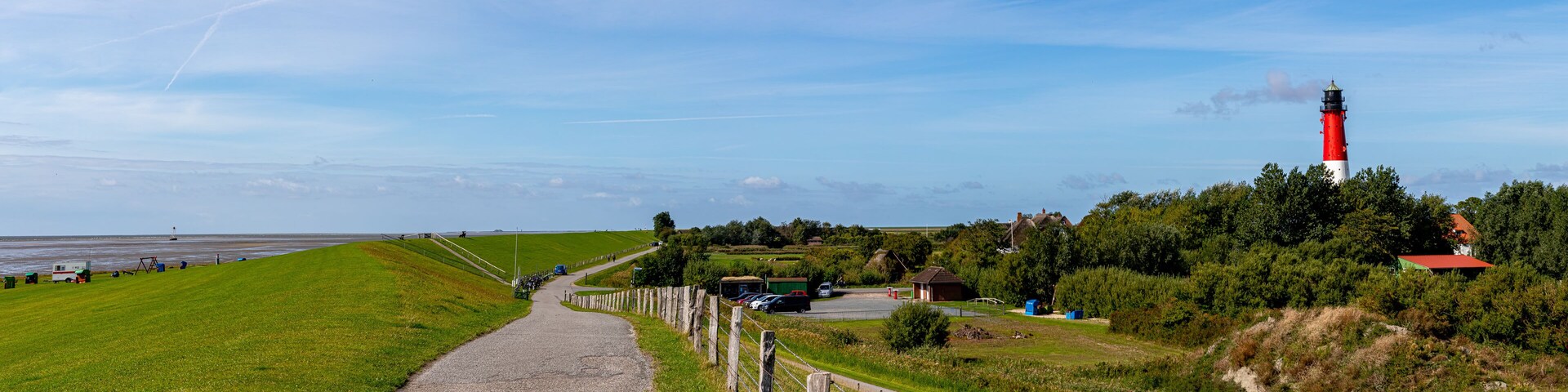 A coastal road with a lighthouse, green fields, and a clear sky.