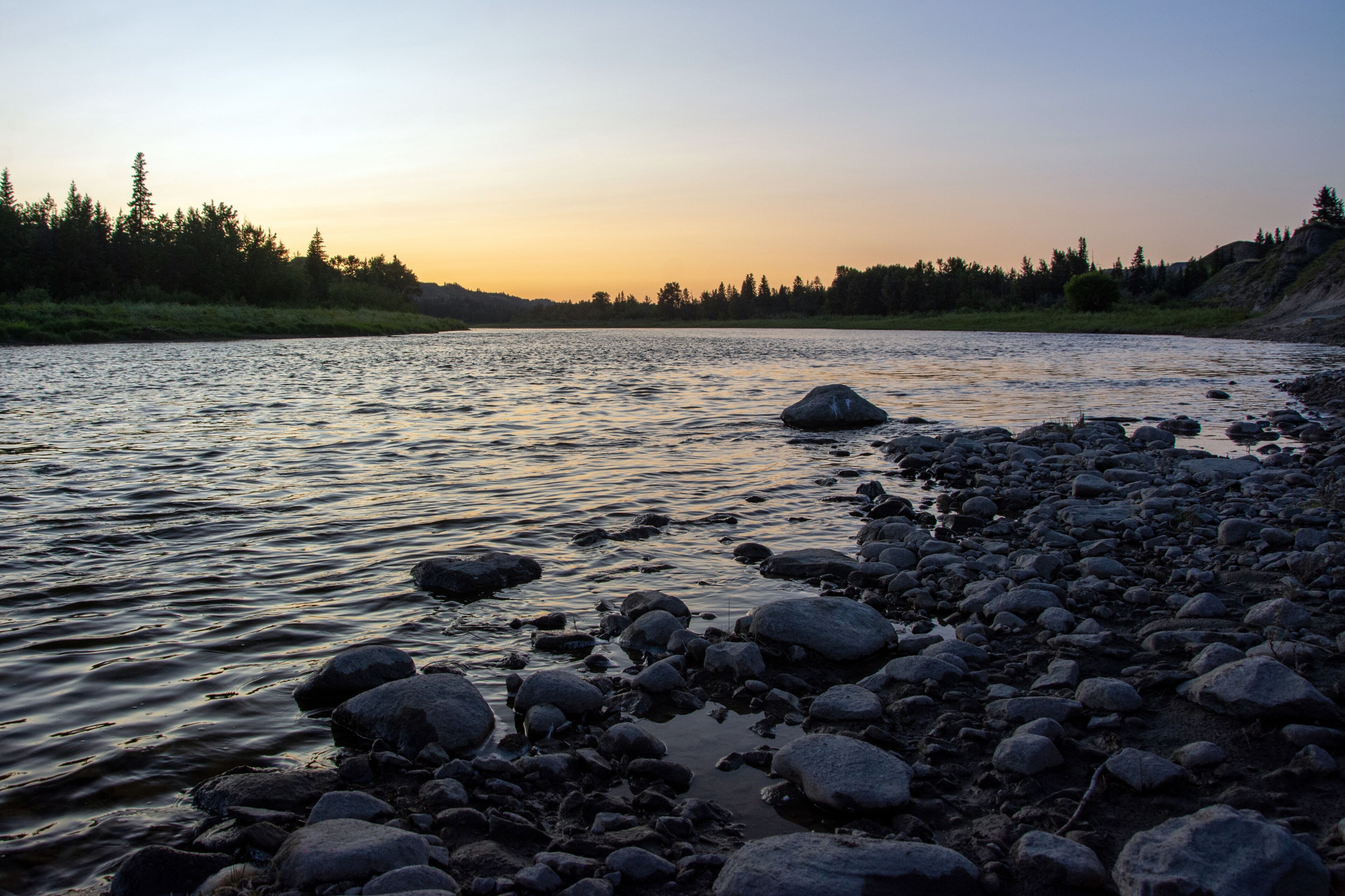 A river with rocks and trees at sunset.