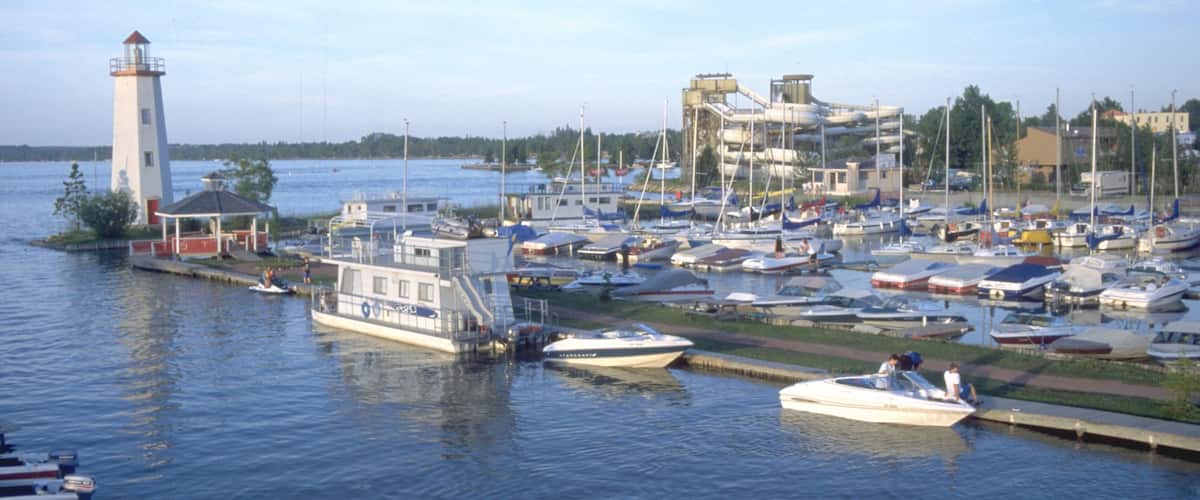 A marina with boats docked, a lighthouse, and a building with a sloped roof.