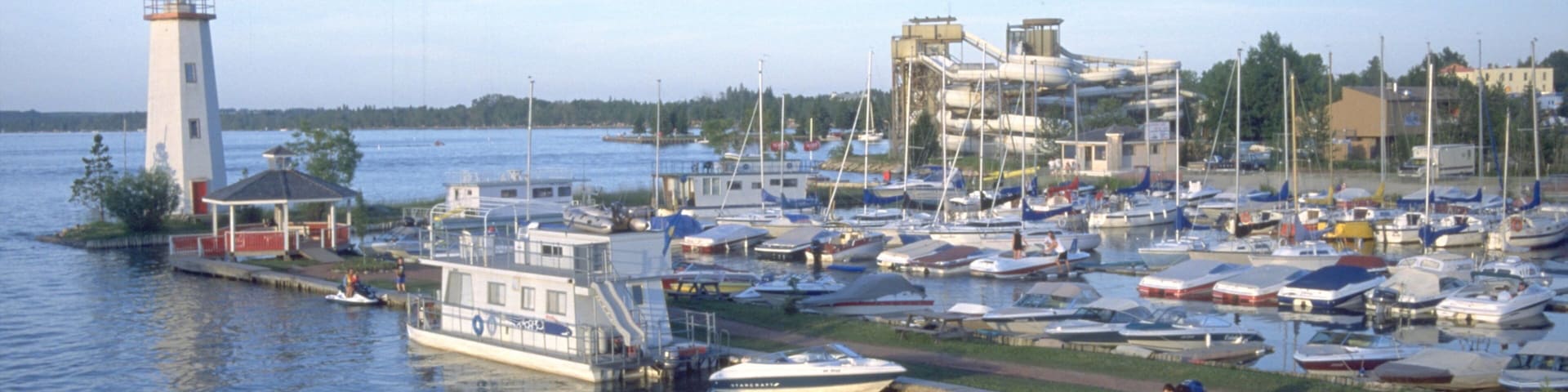 A marina with boats docked, a lighthouse, and a building with a sloped roof.
